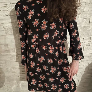 Svart blommig klänning med långa ärmar - Säljer en svart klänning med små blommiga mönster i rött och rosa. Klänningen har långa ärmar och en avslappnad passform med resår i midjan. Perfekt för dig som gillar romantiska och feminina plagg. Pris kan diskuteras.