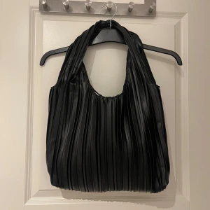 Svart axelväska - Säljer en svart axelväska från Even&Odd i syntetmaterial med snyggt veckad design. Väskan har breda handtag och ett rymligt huvudfack med dragkedja på insidan. 