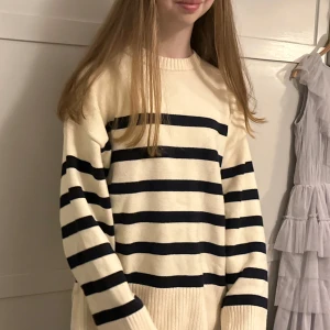 Randig stickad tröja från Zara - Säljer en krämvit stickad tröja från Zara med svarta horisontella ränder. Tröjan har lång ärm, rund halsringning och bred ribbad mudd vid ärmslut och nederkant. Perfekt för en stilren och avslappnad look.