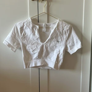 Vit croppad topp från ICIW - Säljer en vit croppad topp från Aim'n med ribbad struktur och korta ärmar. Toppen har en v-ringad hals och är perfekt för en sportig och avslappnad stil.