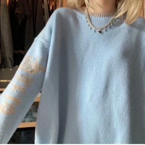 Ljusblå stickad tröja från Chloé - Från Nathalie shuterman ”Chloe schutterman tröjan i ”Paris Säljer en oversized ljusblå stickad tröja från Chloé med beige detaljer. Tröjan har rund halsringning, långa ärmar och ett stort beige tryck på ryggen samt text på ena ärmen. Perfekt för en avslappnad och trendig look.