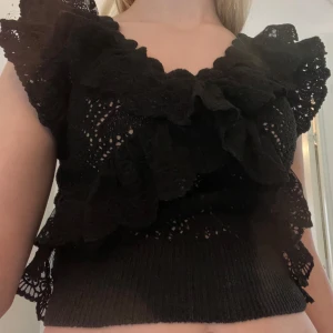 Svart volangblus med spetsdetaljer - Supersöt svart blus med volanger och spetsdetaljer. Djup v-ringning och korta ärmar med volang. Perfekt för att klä upp en enkel outift och funkar både till vardags och till fest  