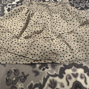 Beige prickig croppad topp - Söt croppad topp i beige med svarta prickar och smock upptill. Luftig och voluminös modell som passar perfekt till sommaren. Toppen har en volangig känsla och är ärmlös.