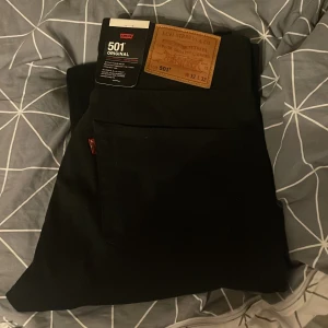 Svarta Levi's 501 Premium jeans - Säljer ett par svarta Levi's 501 Premium jeans i klassisk rak modell. Byxorna har knäppning med knappar, fem fickor och den ikoniska läderpatchen bak. Perfekta för dig som gillar tidlös stil och vill ha ett par jeans som funkar till allt. Helt nya aldrig använda säljer pga att dom inte passade. Kom dm för mer frågor eller bilder!!