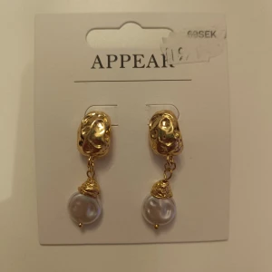 Guldiga örhängen  - Säljer ett par eleganta örhängen från Appear i guld med hängande vita pärlor. Örhängena är aldrig använd!! Nypris 69, mitt pris 25!!proset kan diskuteras 
