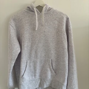 Ljusgrå hoodie från Primark - Mysig ljusgrå hoodie från Primark med huva och dragsko. Tröjan har en stor magficka och är tillverkad i mjukt material, perfekt för avslappnade dagar. Klassisk passform och långärmad modell.