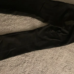 Svarta kostymbyxor - Säljer ett par klassiska svarta kostymbyxor med rak passform. Perfekta att styla med en skjorta eller stickad tröja. Byxorna har enkel design utan synliga detaljer och är tillverkade i ett slätt material. Finns lite knotter på baksidan men det går hur lätt som helst att ta bort!💕