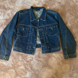 Jeansjacka - Unik blå jeansjacka i mediumtvätt med silverfärgade knappar och två fickor. Jackan har lång ärm, markerad krage och kontrastsömmar. Kontakta mig för mått och frågor 💕