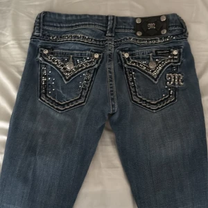 Miss me jeans bootcut - Säljer ett par lågmidjade jeansbyxor från Miss Me med snygga strassdetaljer och broderade fickor bak. Byxorna har bootcut-modell och dekorativa knappar samt märke på bakfickan. Perfekta för dig som gillar extra detaljer på dina jeans! De är vintage och säljer de pga att de inte passar mig längre:( 
