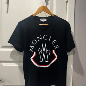Svart Moncler T-shirt - Svart moncler T-shirt med logga på framsidan och på armen. Den är knappt använd och kommer i storlek S. Skriv gärna för fler bilder eller om ni har andra frågor!