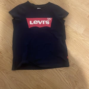 Mörkblå t-shirt från Levi's med logga - Mörkblå t-shirt från Levi's med den klassiska röda och vita loggan tryckt på bröstet. T-shirten har rund halsringning och korta ärmar. Perfekt för en avslappnad och stilren look.