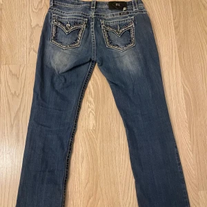 Blå jeansbyxor från Miss Me med dekorerade bakfickor - Jeans från Miss Me med snygga slitningar och dekorerade bakfickor med pärldetaljer. Byxorna har en easyboot passform och är perfekta för dig som gillar detaljer och en cool look 💕