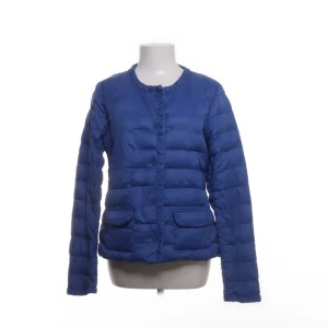 Blå pufferjacka - Snygg blå pufferjacka med rund halsringning och två framfickor. Jackan har långa ärmar och stängs framtill. Perfekt för kyliga dagar när du vill hålla dig varm och se cool ut.