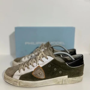 Philippe Models - Snygga gröna sneakers från Philippe Model med vita och svarta detaljer. Skorna har en klassisk snörning och en unik logotyp på sidan. Har använts, men ska även se slitna ut i modellen. Lådan ingår inte har tappat den