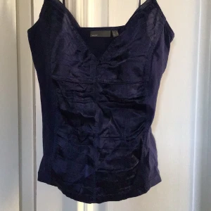 Mörkblå linnetopp från Mexx - Snygg mörkblå linnetopp från Mexx med smala axelband och v-ringning. Toppen har en elegant glansig finish och är perfekt för en stilren look. Passar bra till både jeans och kjol.