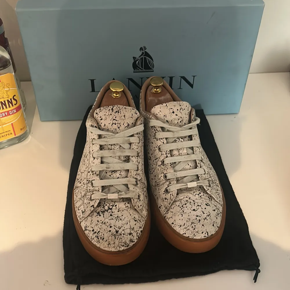 Snygga sneakers från Lanvin i en unik vit och svart mönstrad design. Skorna har en brun sula och klassisk snörning. Perfekta för att ge din outfit en stilfull touch.. Kengät.