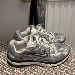 Nike p6000 - Snygga Nike sneakers i en cool kombination av silver och vitt. Skorna har en sportig design med snörning och en bekväm sula. Perfekta för både träning och vardagsbruk.