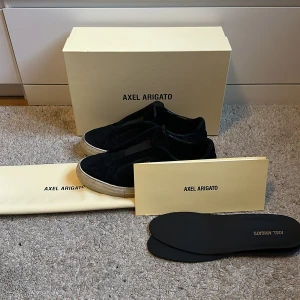 Svarta sneakers från Axel Arigato - Snygga svarta sneakers från Axel Arigato med vit sula och diskret gulddetalj på sidan. Skorna har en stilren design och kommer med originalförpackning och skopåse. Perfekta för en trendig look. Priset är inte hugget i sten! Träffas helst i Stockholm.