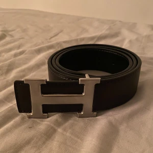 Svart bälte med silverfärgat spänne - Snyggt svart bälte i skinn med ett stilrent silverfärgat H-format spänne. Perfekt för att ge en elegant touch till din outfit. Bältet har en klassisk design och passar till många olika stilar.(priset kan diskuteras)