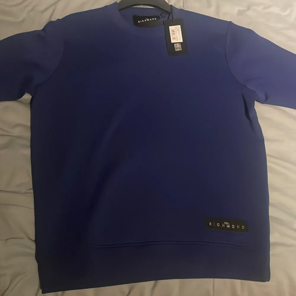 Säljer en stilren blå tröja från John Richmond. Tröjan har en enkel design med en diskret logga på framsidan. Perfekt för en avslappnad look. Helt ny med prislapp kvar. Neuletakit & Villapaidat.