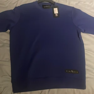 Blå tröja från John Richmond - Säljer en stilren blå tröja från John Richmond. Tröjan har en enkel design med en diskret logga på framsidan. Perfekt för en avslappnad look. Helt ny med prislapp kvar