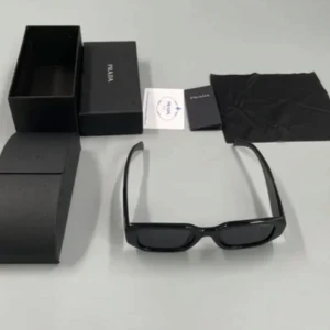 Svarta solglasögon från Prada - Snygga svarta solglasögon från Prada med en rektangulär form. De har en stilren design med breda skalmar där Prada-loggan är synlig. Perfekta för en trendig look.