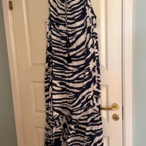 Hollister Zebramönstrad långklänning - Snygg zebramönstrad långklänning i blått och vitt. Klänningen är ärmlös och har en avslappnad passform med knytband vid halsen. Perfekt för en somrig look!