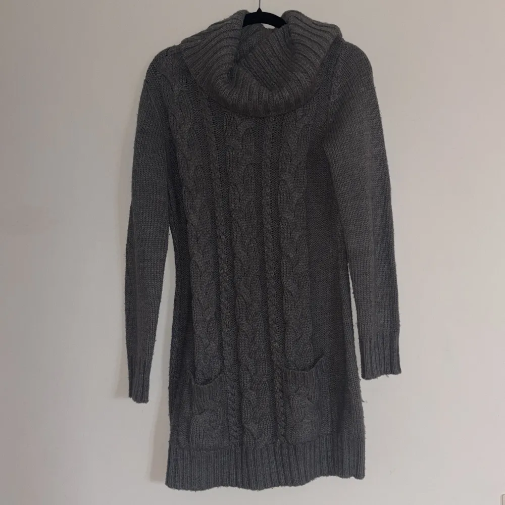 Säljer en mysig grå stickad klänning från Bonprix med kabelstickat mönster och stor krage. Tröjan har långa ärmar och praktiska fickor framtill. Perfekt för kyliga dagar! 🧶. Mekot.