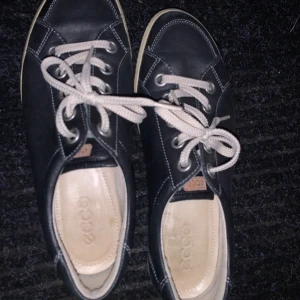 Svarta sneakers från Ecco - Snygga svarta sneakers från Ecco med vita snören och kontrasterande sömmar. Perfekta för en avslappnad stil. Skorna har en klassisk design med rund tå och bekväm passform.