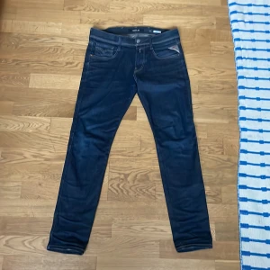 Mörkblå jeans från Replay - Snygga mörkblå jeans från Replay, modell Anbass. De har en slim passform och är tillverkade i ett stretchigt jeansmaterial. Klassisk femficksdesign med knapp och dragkedja framtill. Perfekta för en stilren look. W30 L30