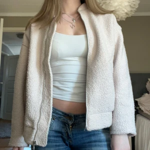 Beige teddyjacka från H&M - Mysig beige teddyjacka från H&M med dragkedja framtill. Jackan har en normal passform och är perfekt för kyligare dagar. Den är långärmad och har en mjuk, fluffig yta som ger en trendig look.