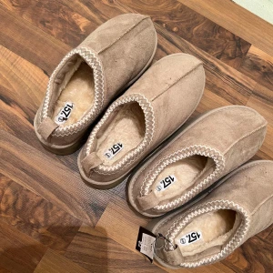 Beige mocka tofflor från 157 - Det är två olika par jag säljer. Storlek 40/41 och 38/39. Vid betalning så får man båda. Ena paret är helt oanvända och det andra är använda en gång. Mysiga beige tofflor i mocka från 157 med mjukt foder. Perfekta för att hålla fötterna varma. De har en enkel design med dekorativ söm runt öppningen.
