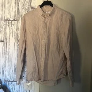 Beige linneskjorta - Säljer en stilren beige skjorta i 100% linne. Skjortan har långa ärmar och knappar framtill, perfekt för en avslappnad men ändå elegant look. Passar bra till både jeans, chinos och alla andra byxor/shorts. Skjortan är aldrig använd så helt nyss skick. Köpt från cubus.