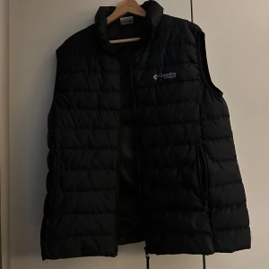 Columbia väst - Säljer en svart väst från Columbia. Västen har en skön svart färg och sitter lite brett vid undersidan annars inga fel förutom att loggan är lite av. Skriv vid minsta fundering.