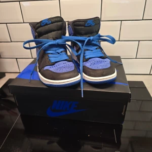Nike Air Jordans i svart och blått - Snygga Nike Air Jordans i svart och blått med klassisk snörning. Skorna har en cool design med blå sula och detaljer, perfekt för en sportig look. Levereras i originalkartong.