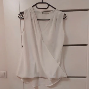 Vit blus med fin hängdetalj - Säljer en stilren vit blus i ett tunt material. Blusen är ärmlös och har en elegant v-ringning. Perfekt för en elegant och avslappnad look. Passar bra till både jeans och kjol. Passar S/M. 