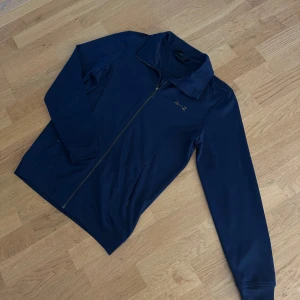 Mörkblå jacka från A-Z - Säljer en stilren mörkblå jacka från A-Z med dragkedja framtill. Jackan har en klassisk krage och långa ärmar. Perfekt för en avslappnad look.