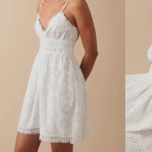 Vit klänning med spetsdetaljer  - Söt vit klänning med smala axelband och spetsdetaljer. Den har en smockad midja och ett vackert broderat mönster. Perfekt för sommarens varma dagar.