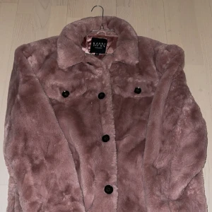 Rosa pälsjacka från MAN - Säljer en supermjuk och stilren rosa pälsjacka från BOOHOO MAN. Jackan har en klassisk krage och knäpps med svarta knappar framtill. Perfekt för att hålla sig varm och trendig under kyliga dagar.