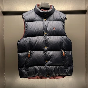 Vändbar dunväst från Ralph Lauren - Snygg vändbar dunväst från Ralph Lauren i marinblått och vinrött. Västen har broderad logga på båda sidor och stängs med knappar. Perfekt för att hålla värmen med stil. Storlek M men passar fint på S också.