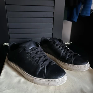 Axel Arigato skor  - Snygga svarta sneakers från Axel Arigato med klassisk design. Skorna har en vit sula och svart snörning som ger en stilren look. Perfekta för en avslappnad stil. Skick: 7/10. Dustbagen följer med