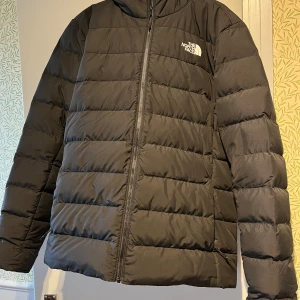 Svart pufferjacka från The North Face - Säljer en svart pufferjacka från The North Face. Jackan har en dragkedja framtill och en hög krage för extra värme. Perfekt för kyliga dagar med sin vadderade design. Huvan ger extra skydd mot väder och vind. Den är som nyskick. Pris kan diskuteras!❤️