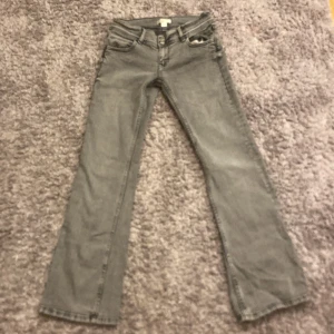 Grå jeans från Gina Tricot - Snygga grå jeans från Gina Tricot med en stjärndetalj på bakfickan. De har en klassisk femficksdesign och en utsvängd passform. Perfekta för en avslappnad stil.