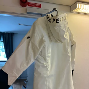Vit skidjacka från Peak Performance - Säljer en vit fodrad skidjacka från Peak Performance med svarta detaljer. Jackan har en huva och dragkedja framtill!  Använd endast 2 gånger