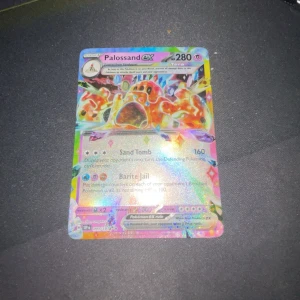 Palossand ex Pokémonkort - Säljer ett holografiskt Palossand ex Pokémonkort med 280 HP. Kortet har attacker som Sand Tomb och Barite Jail. Perfekt för samlare eller spelare som vill förstärka sin kortlek med ett kraftfullt kort.