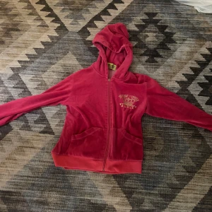 Rosa hoodie från Juicy Couture - Säljer en snygg rosa vintage hoodie från Juicy Couture med broderad text 'Preppy Royalty' och en krona på bröstet. Den har dragkedja framtill och en mysig huva. Dock så har den lilla saken man drar i ramlat av men de funkar att dra upp den ändå. 