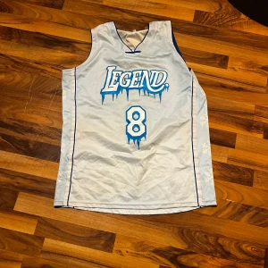 Vit ärmlös baskettröja med blå detaljer - Säljer en vit ärmlös baskettröja med blå detaljer och texten 'Legend' samt siffran 8 på framsidan. Baksidan har namnet 'Bryant' och siffran 24. Perfekt för basketfans!