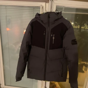 Sailracing Vinterjacka  - Säljer en grymt snygg pufferjacka från Sail Racing i grått, svart med limegrön insida. Otroligt bra på att hålla värmen vid extrem kyla och en perfekt vinterjacka. Därtill har den sex stycken rymliga fickor. Bra skick, inte så gammal, finns dock lite skrapskador under armarna men det är inget som syns. Perfekt för vinter!