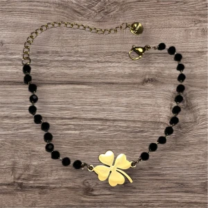 Svart och guld armband med fyrklöver - Helt nytt! Elegant armband med svarta pärlor och en guldpläterad fyrklöver i mitten. Justerbar kedja med klolås för perfekt passform. Perfekt för att ge en touch av lycka och stil. En storlek 16-21 mm