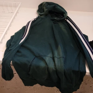 Grön hoodie med ränder från Cubus - Mörkgrön hoodie från Cubus i ekologisk bomull. Tröjan har huva med snörning, vita och svarta ränder längs ärmarna och en stor magficka. Perfekt för chill dagar eller när du vill ha en sportig look.